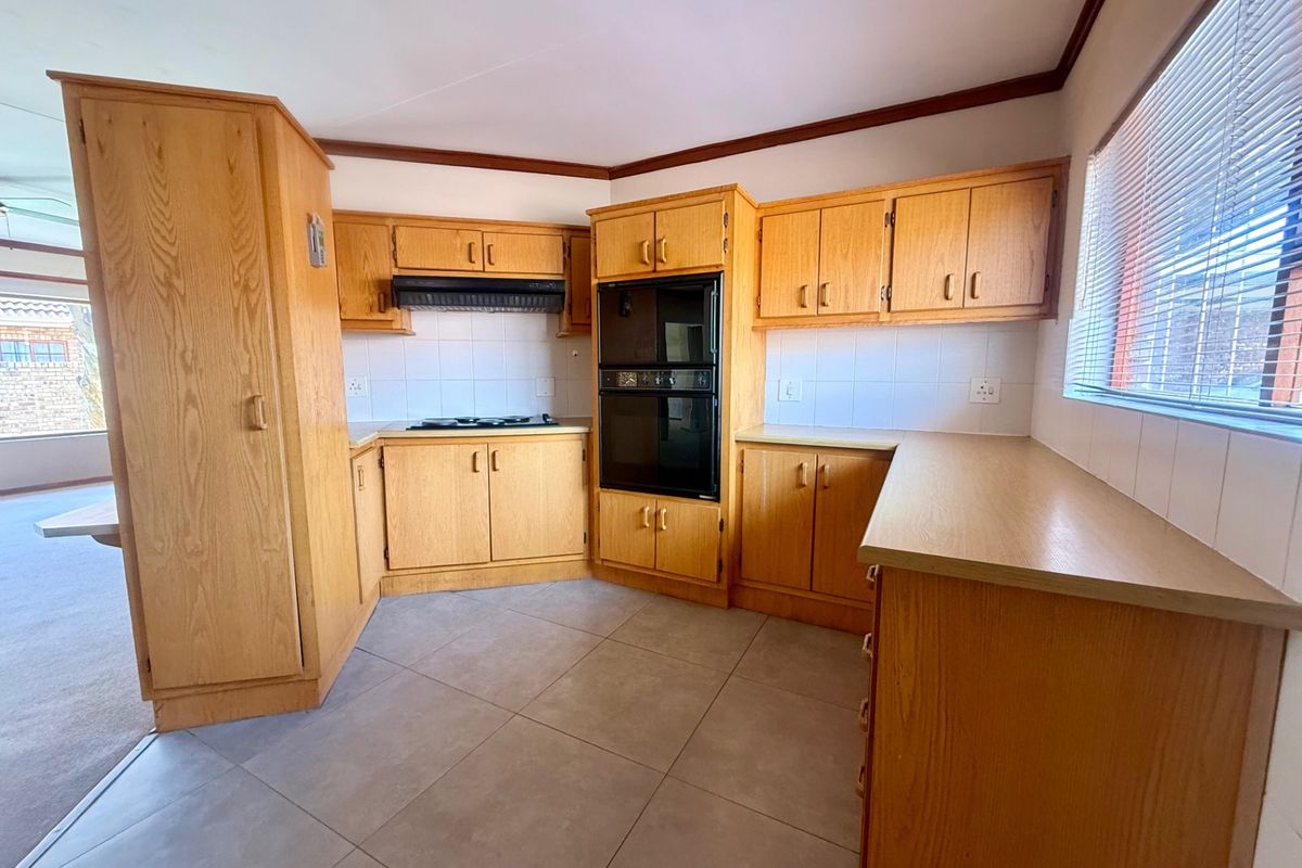 A functional kitchen featuring wooden cabinetry, built-in double oven, hob, extractor fan, and tiled flooring, offering a classic layout ready for modernization.