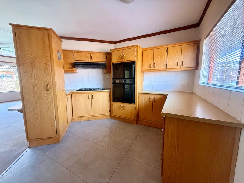 A functional kitchen featuring wooden cabinetry, built-in double oven, hob, extractor fan, and tiled flooring, offering a classic layout ready for modernization.
