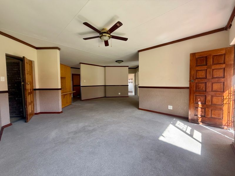 Spacious, empty living area featuring a ceiling fan, traditional wooden doors, and dado rail detailing, offering a blank canvas for renovation.
