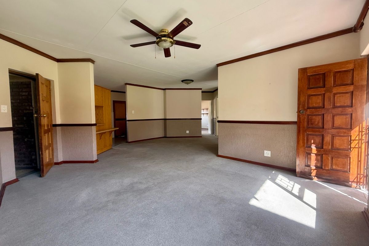 Spacious, empty living area featuring a ceiling fan, traditional wooden doors, and dado rail detailing, offering a blank canvas for renovation.