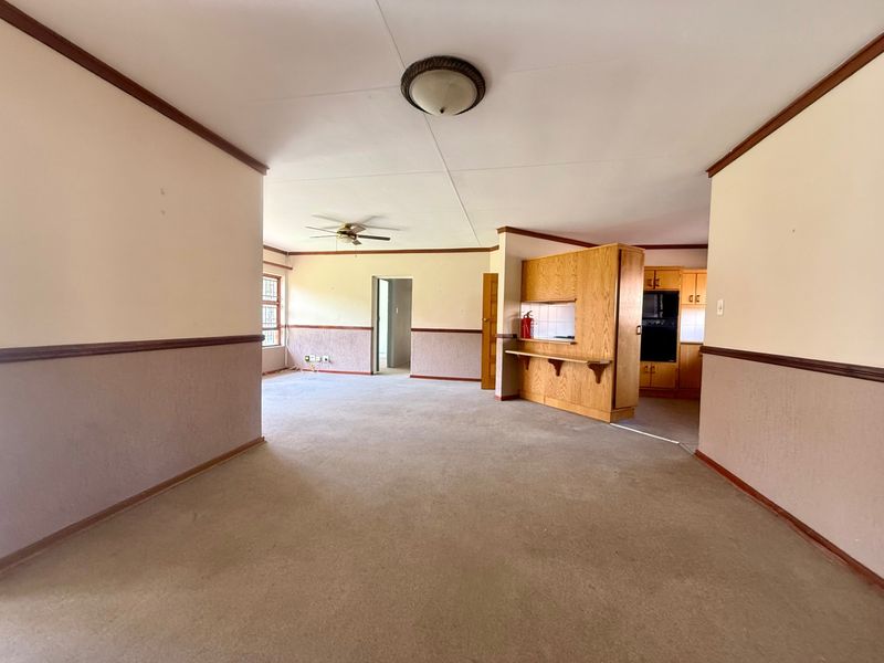 Spacious open-plan living and kitchen area featuring dated cabinetry, carpeted flooring, and a neutral color palette, offering significant potential for modernization.