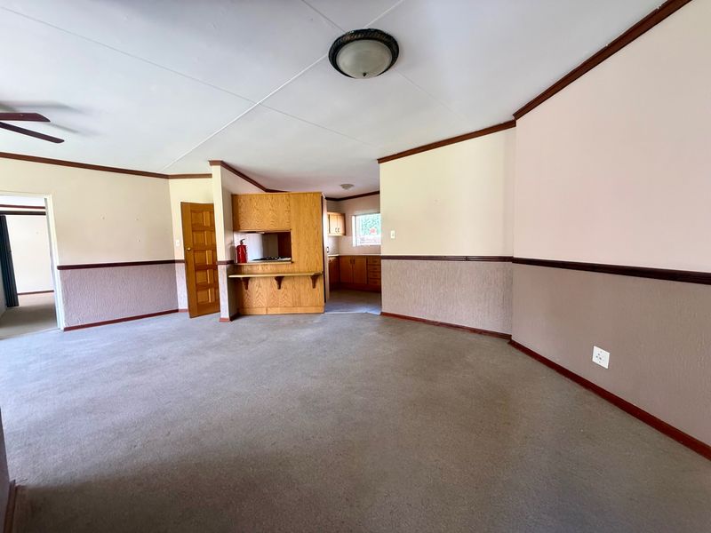 Spacious open-plan living area featuring neutral walls, carpeting, and a functional kitchen pass-through, offering a blank canvas for renovation and modernization.