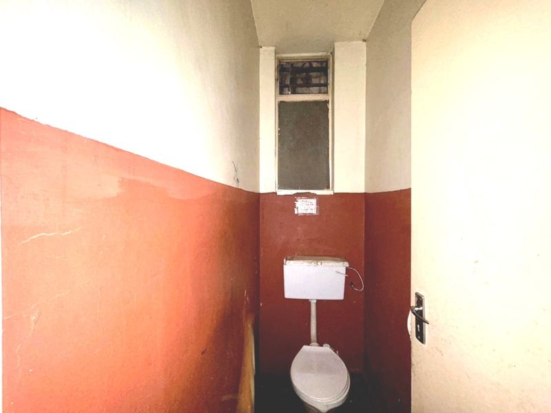 A small, dated bathroom featuring a basic toilet and high-level window, requiring significant cosmetic updates and refurbishment to improve its condition.