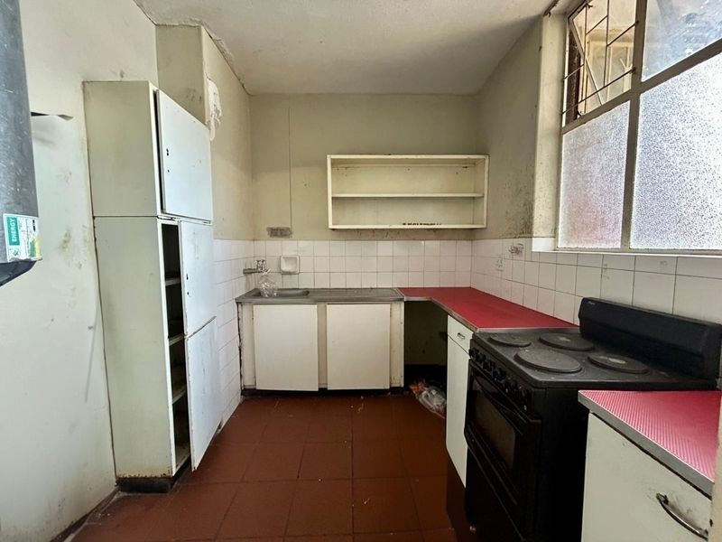 A dated kitchen featuring tiled splashbacks, basic cabinetry, and a freestanding stove, requiring significant renovation and cosmetic updates to improve functionality and aesthetic appeal.