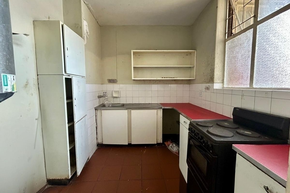 A dated kitchen featuring tiled splashbacks, basic cabinetry, and a freestanding stove, requiring significant renovation and cosmetic updates to improve functionality and aesthetic appeal.