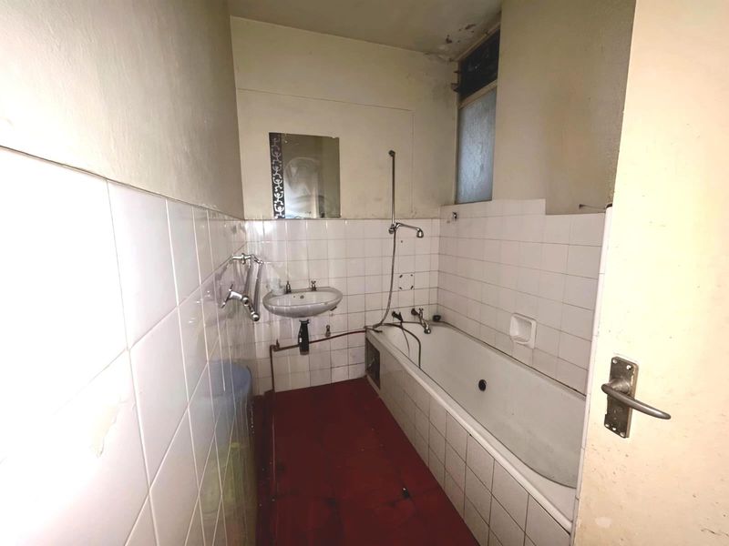 A dated bathroom featuring a bathtub, wall-mounted basin, and tiled finishes, currently in need of renovation and cosmetic updates.