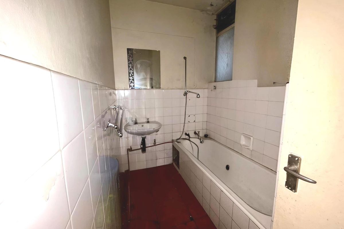 A dated bathroom featuring a bathtub, wall-mounted basin, and tiled finishes, currently in need of renovation and cosmetic updates.