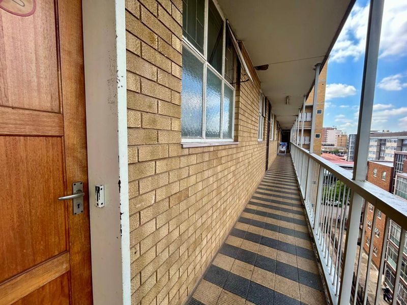 An exterior apartment balcony featuring brick wall finishes, tiled flooring, and a metal safety balustrade overlooking the surrounding urban area.