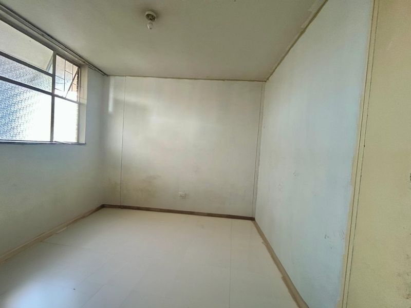 An empty bedroom featuring tiled flooring and a single window, requiring cosmetic updates to the wall finishes and trim.