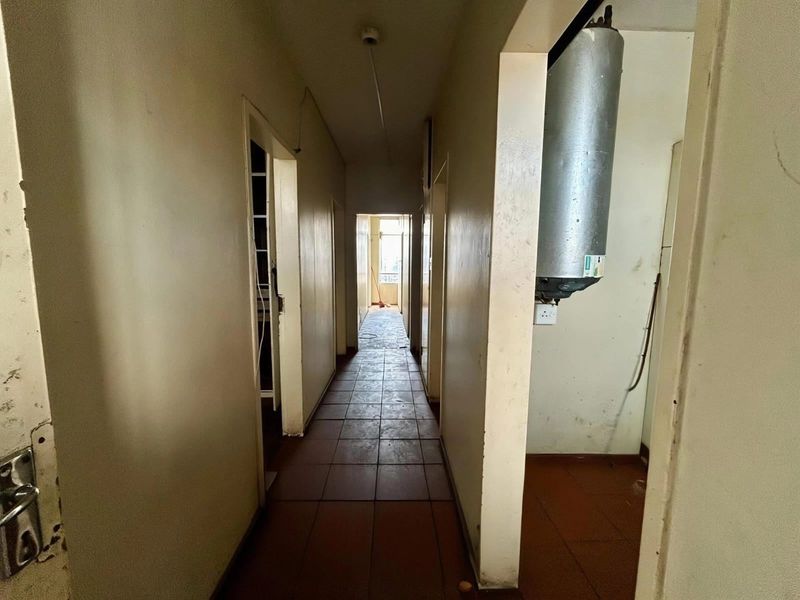 A vacant interior hallway featuring tiled flooring and a wall-mounted electric water heater, requiring cosmetic updates to improve its overall condition.
