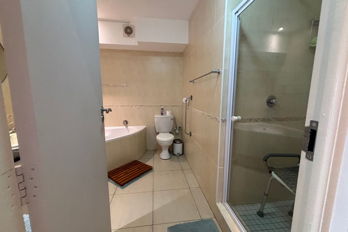 A functional bathroom featuring a corner bathtub, separate shower enclosure, toilet, and neutral wall and floor tiling.