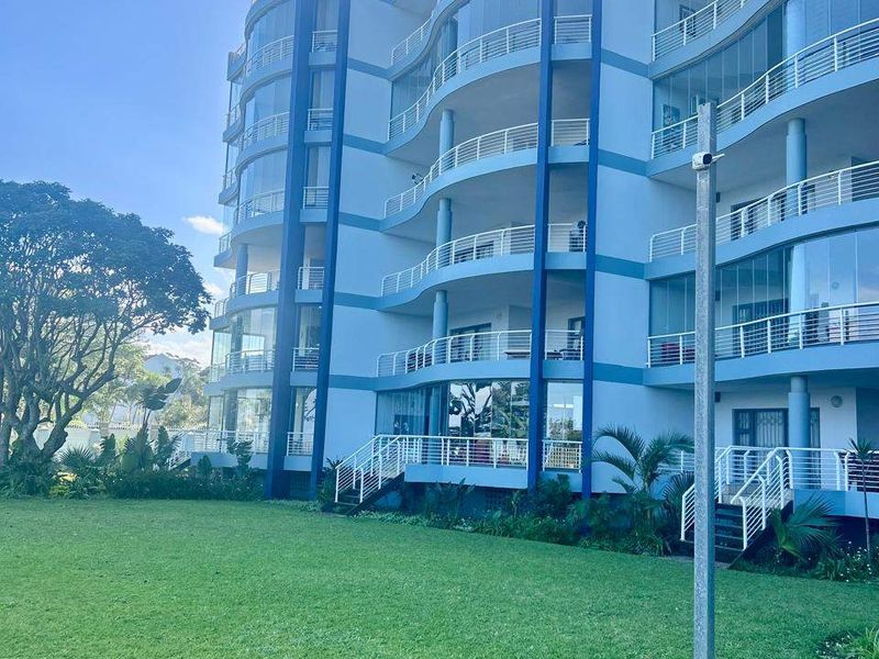 A view of the rear facade of a modern apartment building featuring multiple levels of balconies with glass balustrades overlooking a well-maintained lawn.