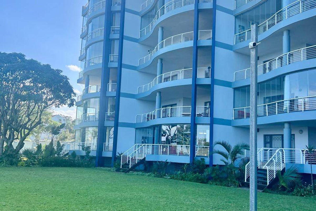 A view of the rear facade of a modern apartment building featuring multiple levels of balconies with glass balustrades overlooking a well-maintained lawn.