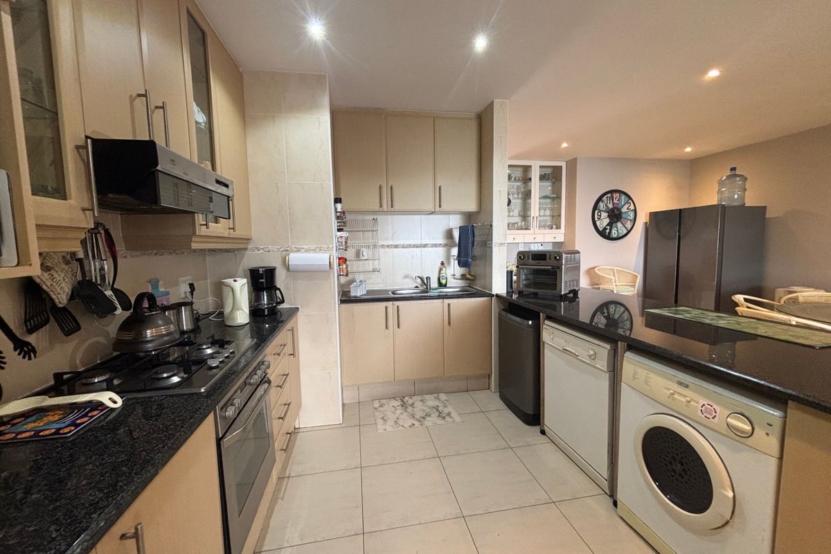 A functional kitchen featuring light wood cabinetry, dark granite countertops, a gas hob, and integrated appliance spaces with tiled flooring throughout.