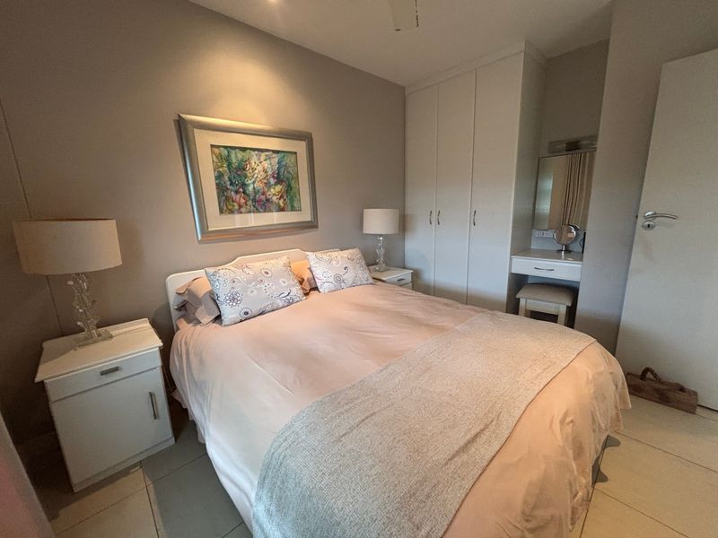 A well-maintained bedroom featuring built-in cupboards, a dedicated vanity area, tiled flooring, and recessed lighting.