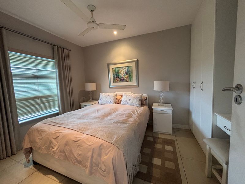 A well-maintained bedroom featuring built-in cupboards, tiled flooring, and a ceiling fan, offering a comfortable and functional living space.
