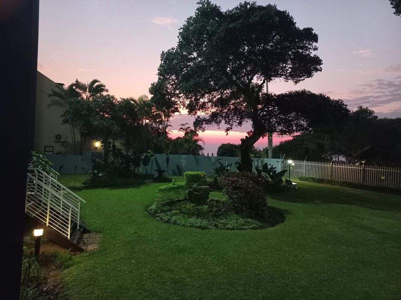 A well-maintained garden area featuring a lush lawn, mature tree, and perimeter fencing, captured during a scenic sunset.