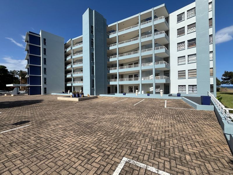 Exterior view of a multi-story apartment building featuring a paved parking area and multiple balconies.