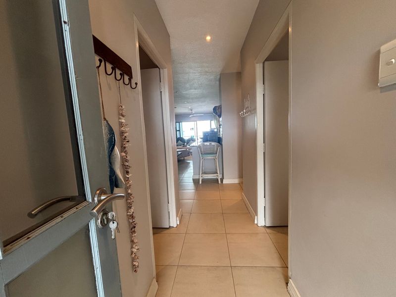 A functional apartment hallway with tiled flooring and recessed lighting, providing access to multiple rooms and leading towards the open-plan living area.