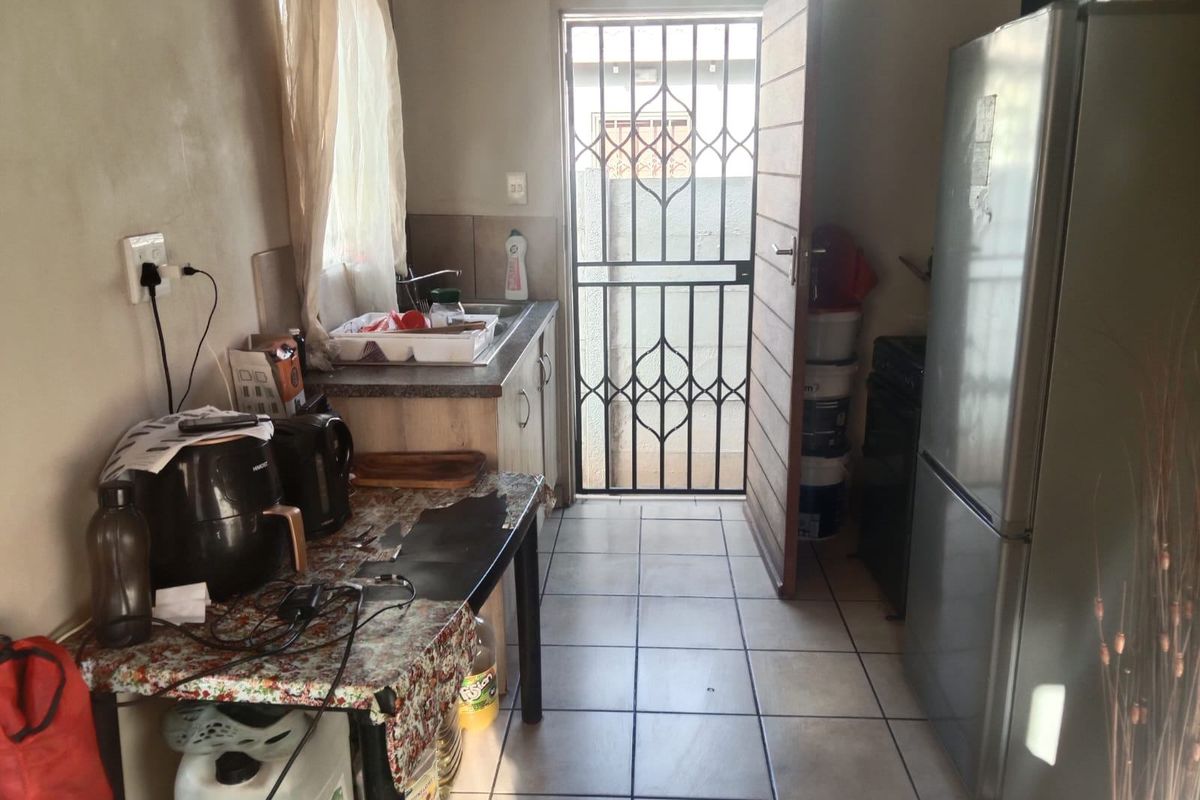 A functional kitchen area featuring tiled flooring, built-in cabinetry, and a secure exterior door with a metal security gate.