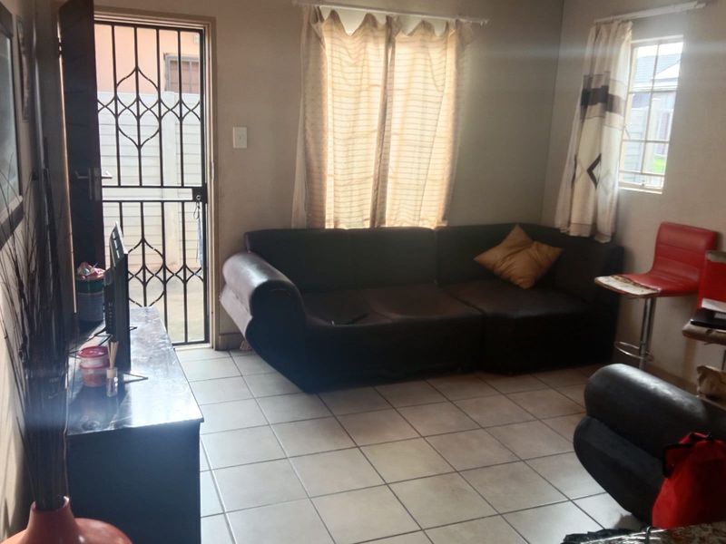 A functional living room area featuring tiled flooring, a security gate at the entrance, and natural light from the window.