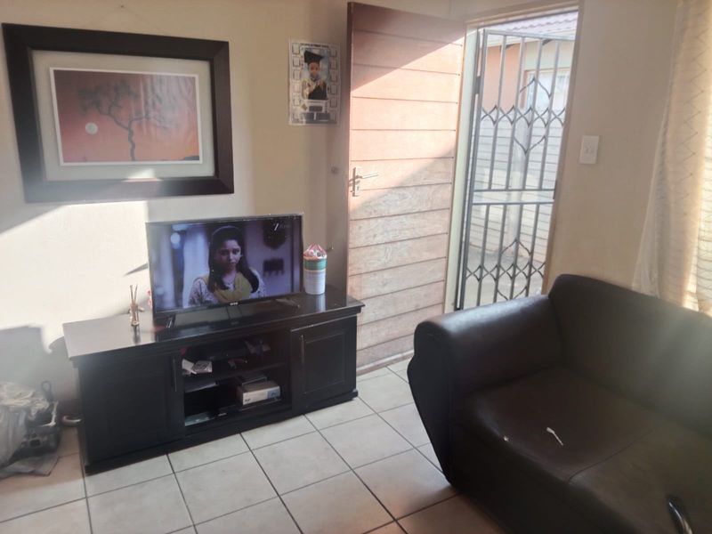 A living room area featuring tiled flooring and direct access to the exterior through a timber door with a security gate.