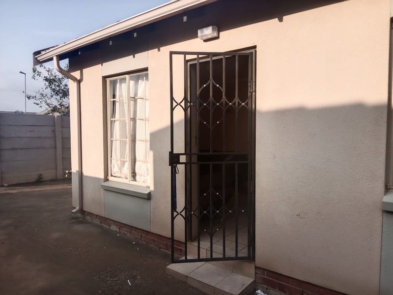 Rear exterior view of the property featuring a security gate, external lighting, and precast boundary walling.