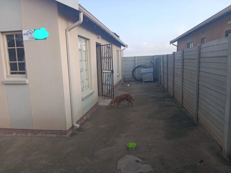 A side exterior view of the property featuring a security gate, precast concrete boundary wall, and concrete paving.