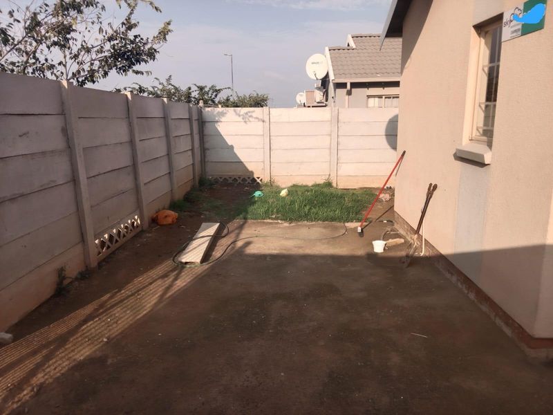 A compact rear yard featuring a concrete patio area and a small grass lawn enclosed by a precast concrete boundary wall.
