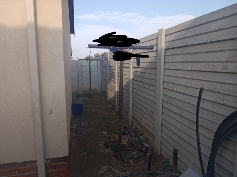 A narrow side or rear yard area featuring a precast concrete boundary wall and an unpaved ground surface.