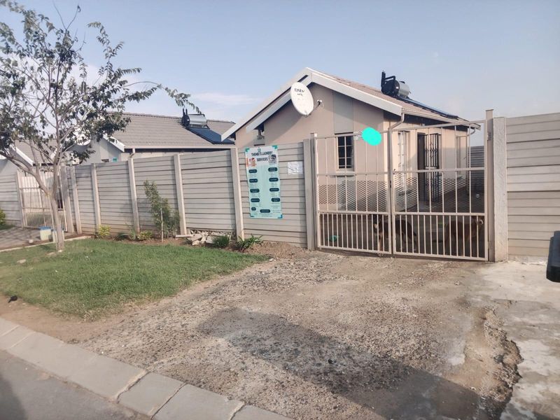 Front exterior view of a residential property featuring a precast concrete boundary wall, metal security gate, and solar water heating system.