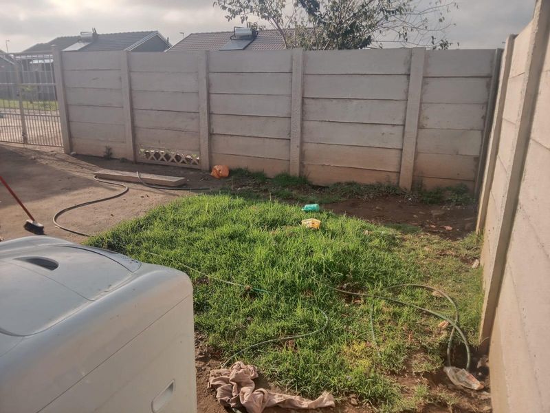 A rear yard area featuring a precast concrete boundary wall and a small patch of lawn, offering potential for landscaping and outdoor improvement.