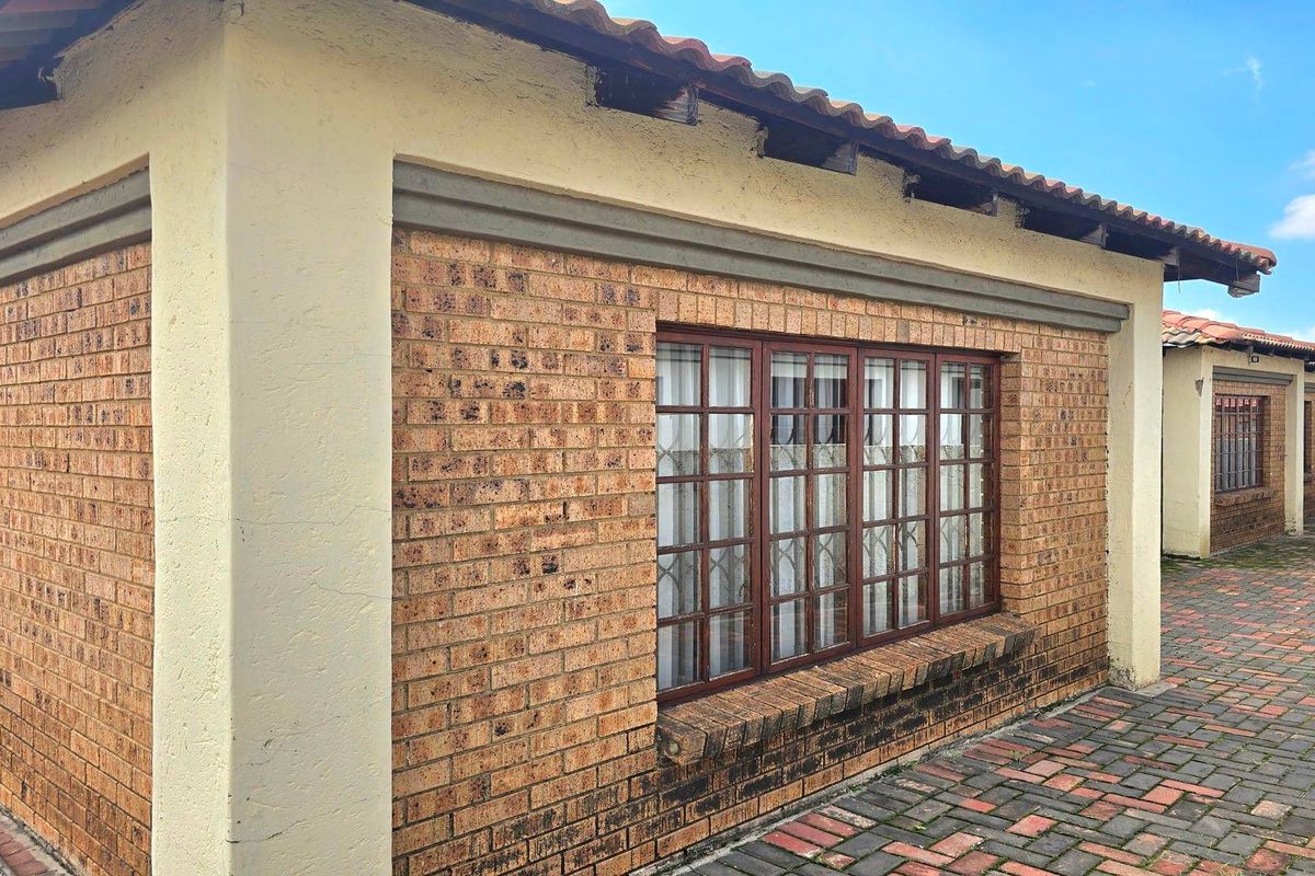 Exterior view of a face brick house featuring a tiled roof, security-fitted windows, and a paved courtyard area.