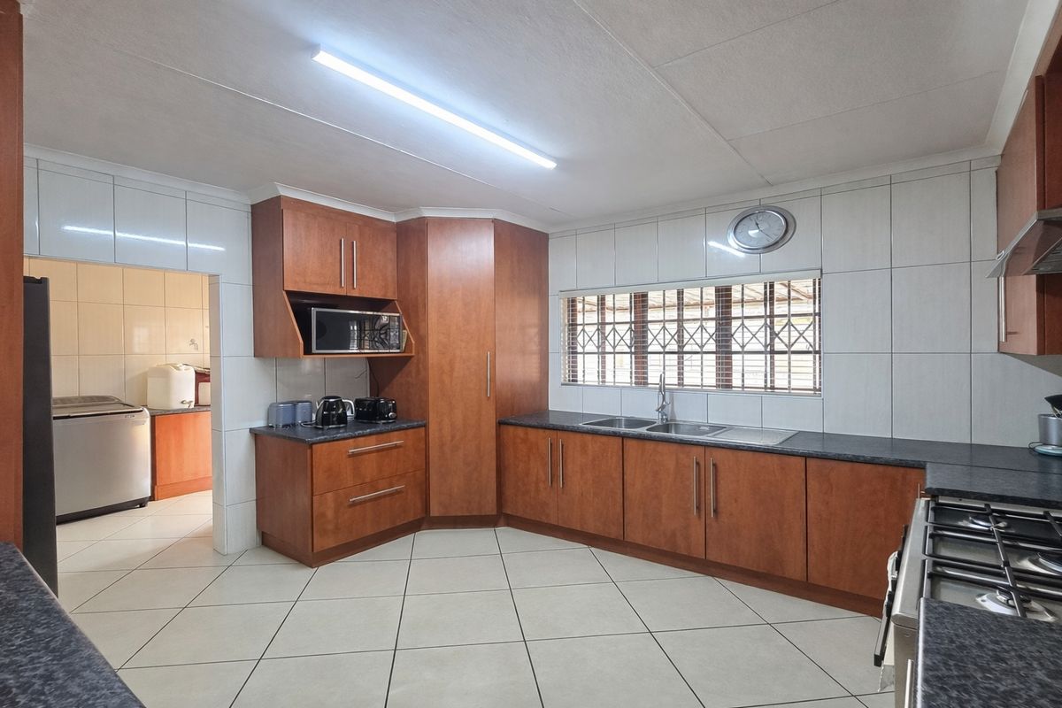 A functional kitchen featuring wood-finish cabinetry, dark laminate countertops, a gas hob, and tiled finishes, with an adjacent scullery area visible.