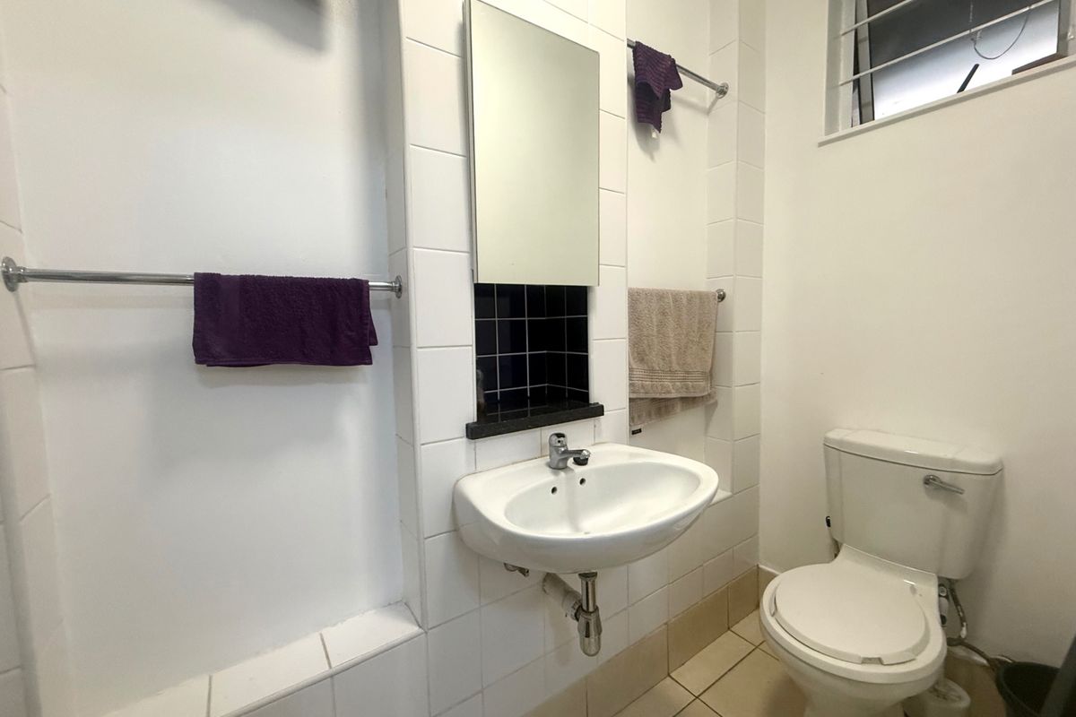 A functional bathroom featuring a wall-mounted basin, toilet, tiled splashback, and recessed shelving with a window for natural light.