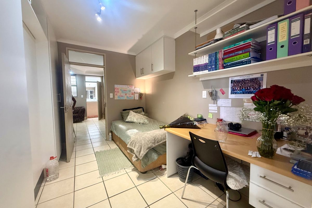 A functional bedroom featuring tiled flooring, built-in desk space, overhead storage cabinets, and built-in cupboards, providing efficient use of space.