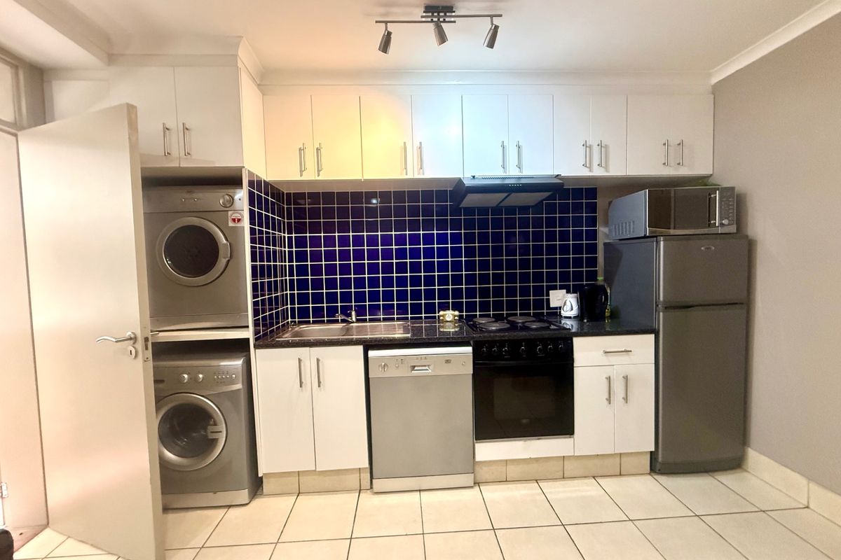 Compact kitchen featuring white cabinetry, dark countertops, blue tiled splashback, and integrated laundry appliances, providing a functional and efficient workspace.