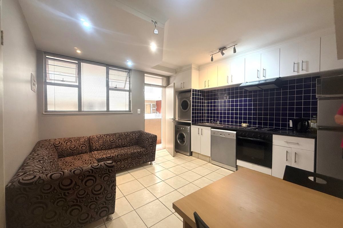 Open-plan living and kitchen area featuring tiled flooring, built-in cabinetry, integrated laundry appliances, and a dark tiled backsplash.