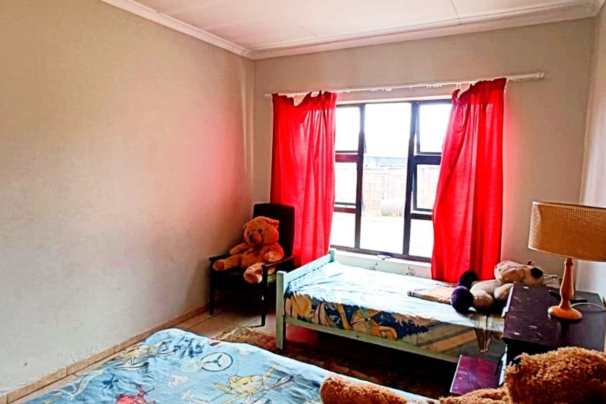 A bedroom featuring a large window with metal frames, neutral wall tones, and standard ceiling cornicing.