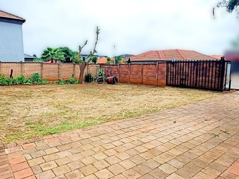 A spacious rear garden featuring a paved driveway, brick boundary walls, and a metal sliding gate, offering potential for landscaping and outdoor improvements.