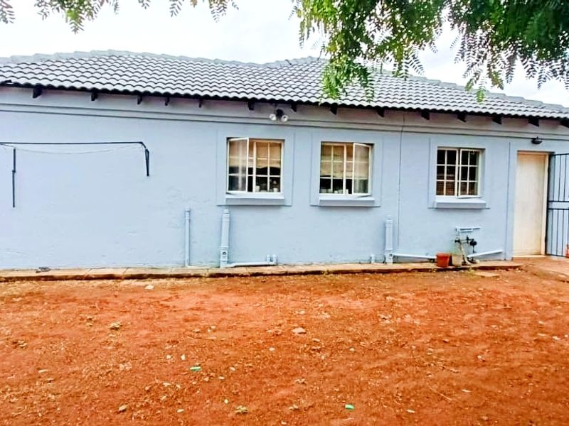 Rear view of the house featuring a tiled roof, security gate, and exterior wall-mounted laundry line, set against an unlandscaped yard.