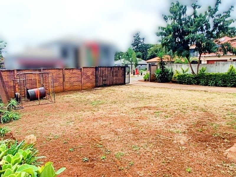 A spacious rear garden area featuring a brick boundary wall, metal gate, and paved walkway, offering potential for landscaping improvements.