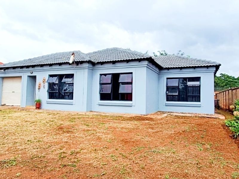 A well-maintained single-story house featuring a tiled roof, grey exterior walls, and dark-framed windows, set on a spacious plot with a front garden.