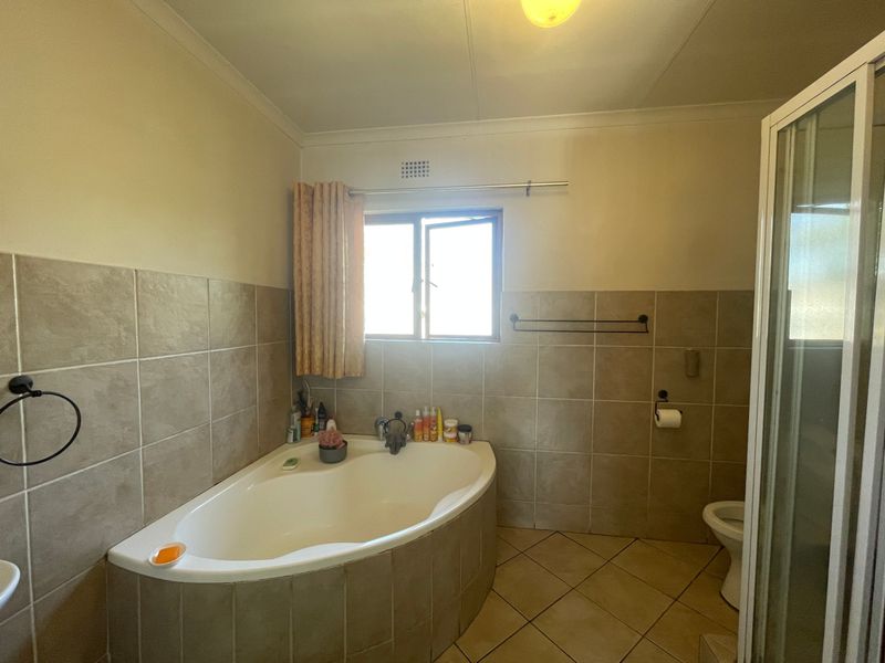 A functional bathroom featuring a corner bathtub, a separate shower enclosure, and neutral wall and floor tiling.