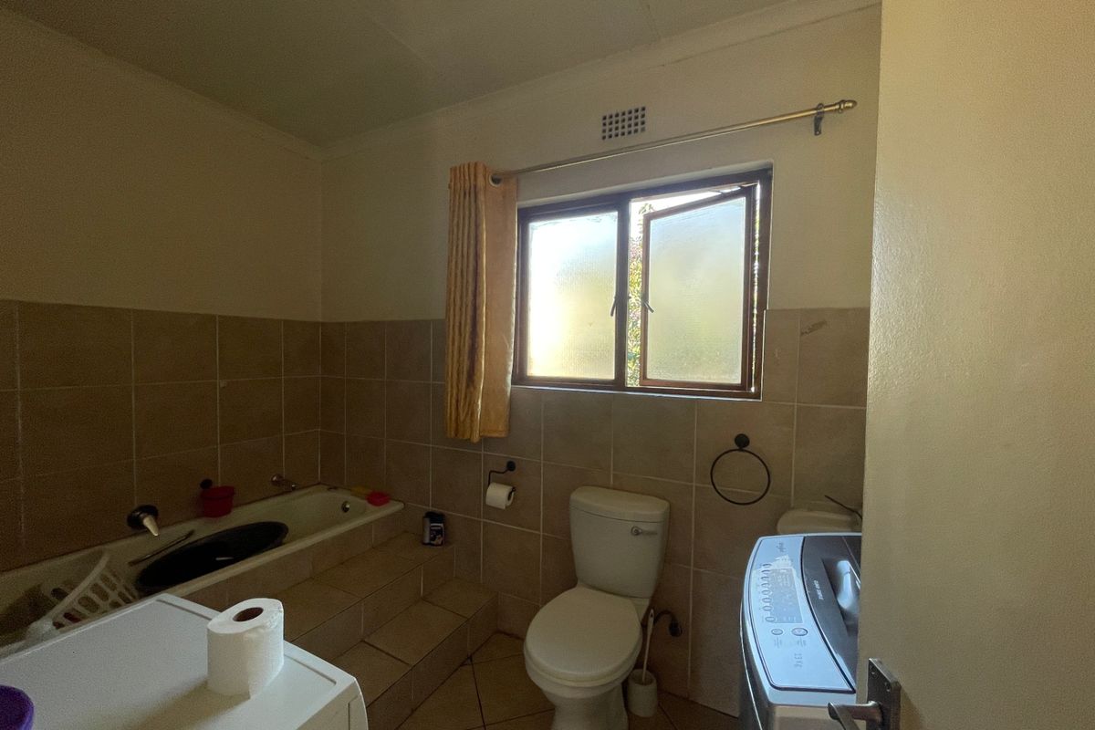 A functional bathroom featuring a built-in bathtub, tiled walls and flooring, and a toilet, requiring cosmetic updates to improve its overall condition.