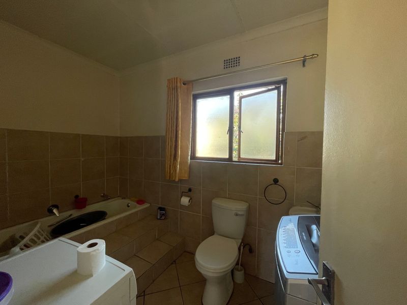 A functional bathroom featuring a built-in bathtub, tiled walls and flooring, and a toilet, requiring cosmetic updates to improve its overall condition.