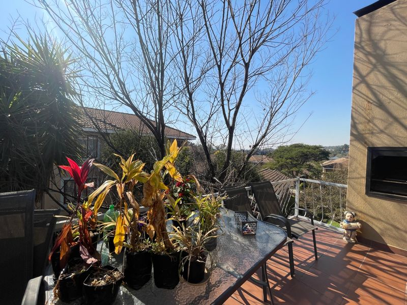 An elevated balcony featuring tiled flooring, a built-in braai, and a metal balustrade with views over the surrounding neighborhood.
