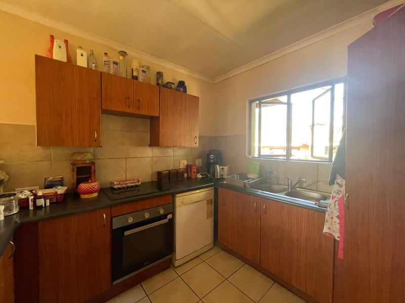 A functional kitchen featuring wood-look laminate cabinetry, built-in oven, hob, double sink, and tiled splashback with natural light from the window.