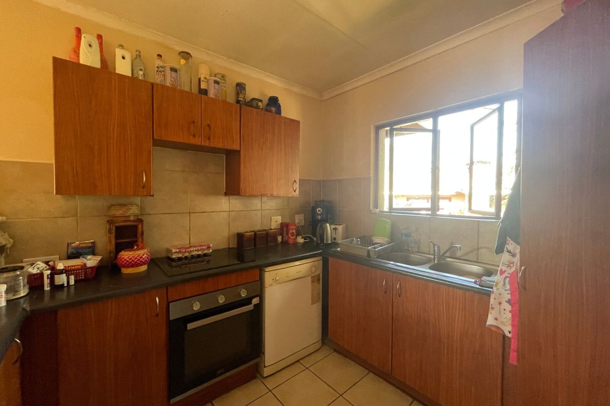 A functional kitchen featuring wood-look laminate cabinetry, built-in oven, hob, double sink, and tiled splashback with natural light from the window.