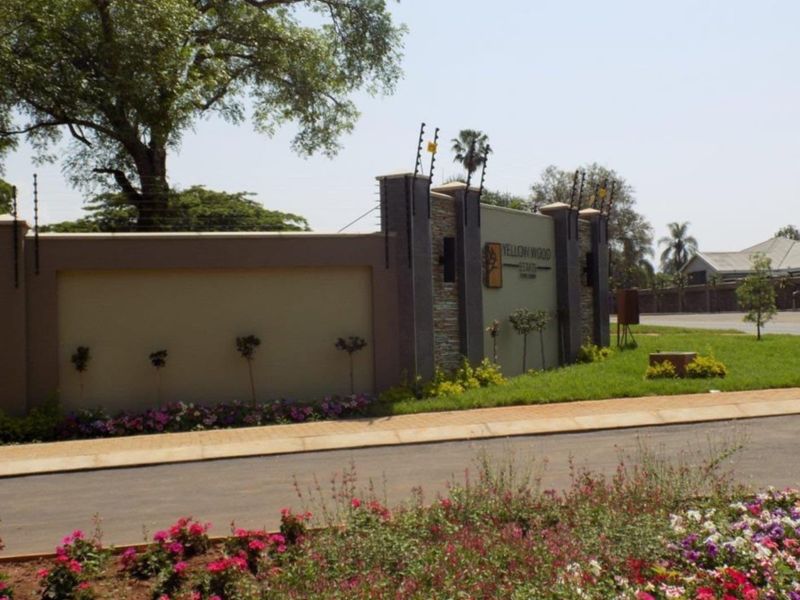 The entrance to Yellow Wood Estate featuring a modern boundary wall with stone cladding, electric fencing, and well-maintained landscaped gardens.